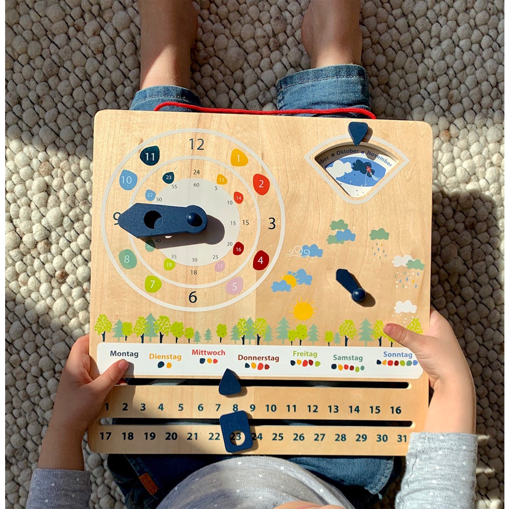 Ein Kind sitzt im Schneidersitz und hält die Lernuhr mit Kalender „Educate“, eine Holztafel mit einer Uhr und bunten Tages- und Wettersymbolen.