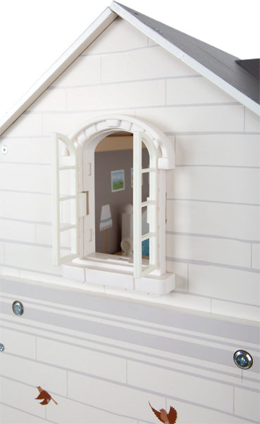 Die Puppenhaus-Stadtvilla hat eine weiße Außenfassade und ein offenes Fenster, in dem Miniaturmöbel ausgestellt sind.