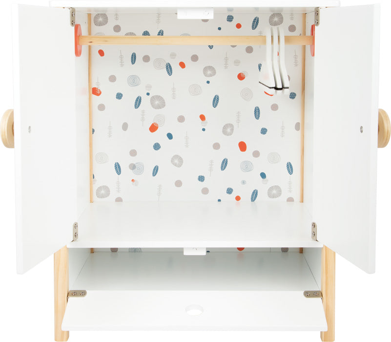 Der Puppenschrank „Little Button“ ist ein offener weißer Schrank mit gemusterter Tapete, einer Kleiderstange und einem unteren Regal im Inneren.