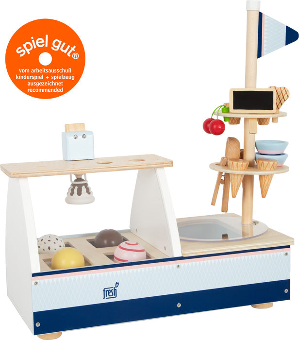 Eistheke „fresh“: Eisstand aus Holz mit Waffeln, Kugeln, Toppings, Fahne und Spiel Gut-Auszeichnungsplakette.
