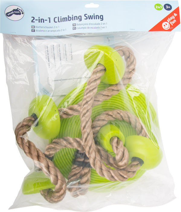 Die Tellerschaukel mit Kletterseil ist ein 2-in-1-Schaukel- und Kletterspielzeug mit grünen Kunststoffteilen und braunen Seilen, sichtbar durch die durchsichtige Verpackung.