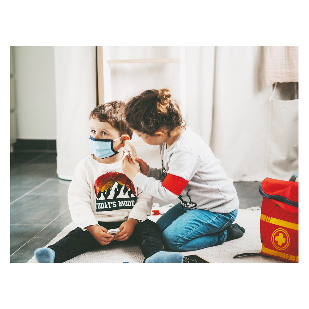 Mit dem Notarztrucksack spielen zwei Kinder Arzt: Einer trägt eine Maske, während der andere so tut, als würde er sein Ohr mithilfe des Spielzeugsets untersuchen.