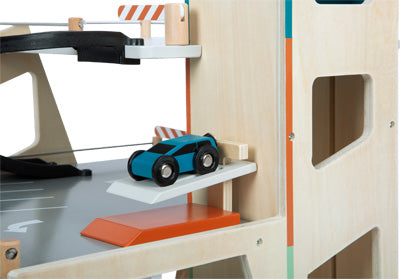 Bei der Parkhaus Rallye steht ein blaues Spielzeugauto auf einer kleinen weißen Rampe in einem hölzernen Spielzeugparkhaus.