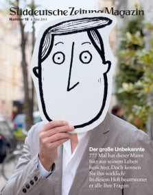 Eine Person hält einen großen Cartoon-Gesichtsausschnitt vor ihr eigenes Gesicht auf einer Stadtstraße.