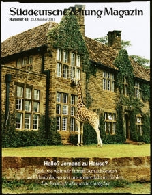 Eine Giraffe steht am Fenster eines großen, mit Efeu bewachsenen Steinhauses mit vielen Fenstern.