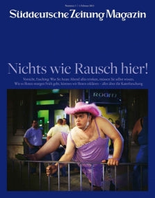 Ein Mann in einem lilafarbenen Kleid und mit rosa Cowboyhut klettert über einen Zaun; im Hintergrund sehen Menschen zu.