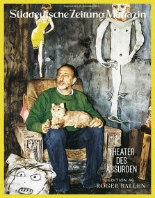 Ein Mann mit einer Katze auf dem Schoß sitzt in einem Sessel, an der Wand hinter ihm hängen surreale Kunstwerke und Zeichnungen.