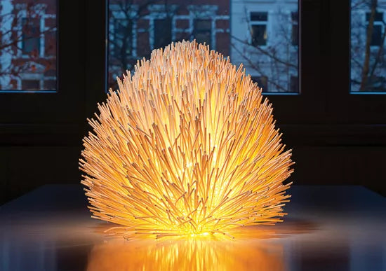 Die Tisch- und Bodenleuchte „Trend“, eine leuchtende, stachelige Lampe, steht auf einem Tisch vor großen Fenstern.