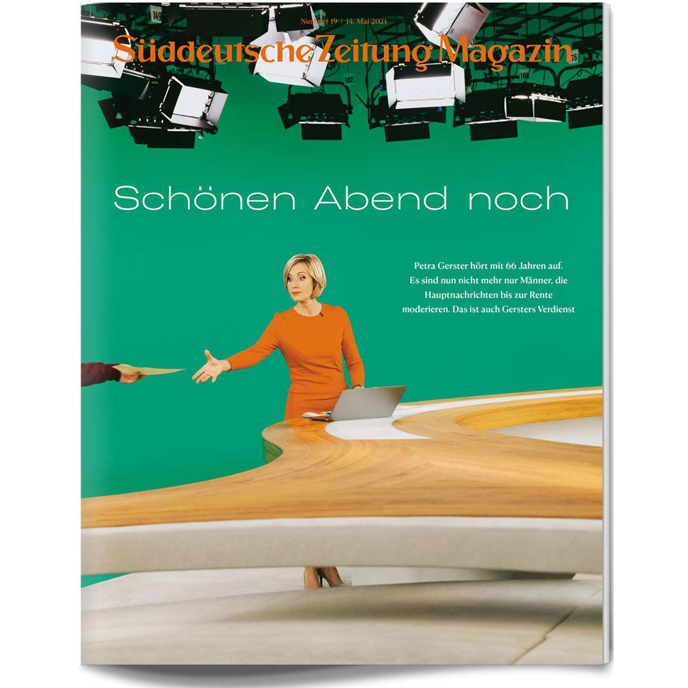 Eine Nachrichtensprecherin in Orange steht an einem Schreibtisch in einem Fernsehstudio mit einem grünen Bildschirm und Kameras über ihr.