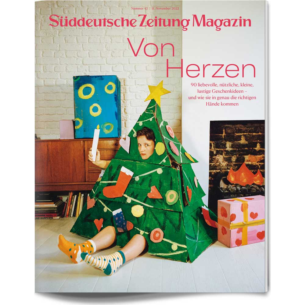 Eine als Weihnachtsbaum verkleidete Person sitzt auf dem Boden und schmückt sich mit Ornamenten; auf dem Titelblatt steht Von Herzen.