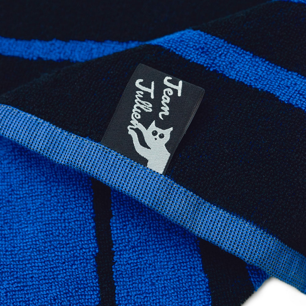 Nahaufnahme eines blau-schwarzen Handtuchs mit einem Jean-Jullien-Etikett mit einer weißen Cartoon-Katze.