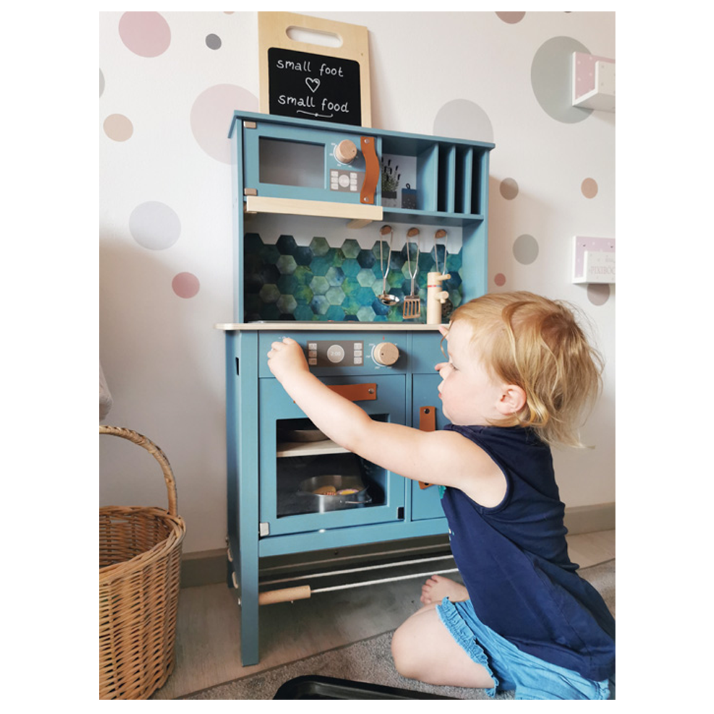 Ein Kleinkind spielt mit dem blauen Spielzeugküchenset „lecker“ von Kinderküche und greift nach der Backofentür, um sie zu öffnen.