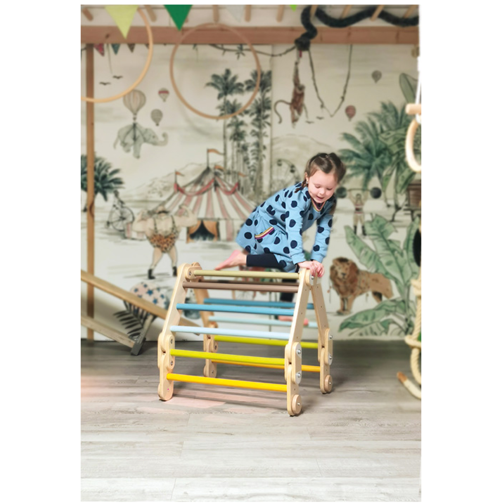 Ein lächelndes Kind erklimmt das Kletterdreieck „Adventure“ in einem Spielzimmer mit einem Wandgemälde zum Thema Zirkus.