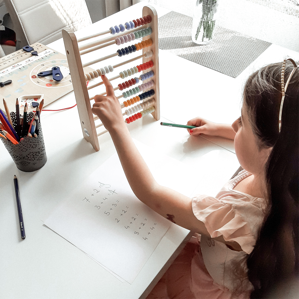 Ein Mädchen löst mit dem Rechenschieber „Educate“ Abakus an einem Tisch mit Bleistift und Papier Matheaufgaben.