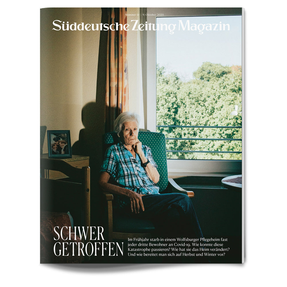 Ältere Frau sitzt allein am Fenster eines Pflegeheims, Sonnenlicht fällt ein, Text auf dem Titelblatt einer Zeitschrift auf Deutsch.