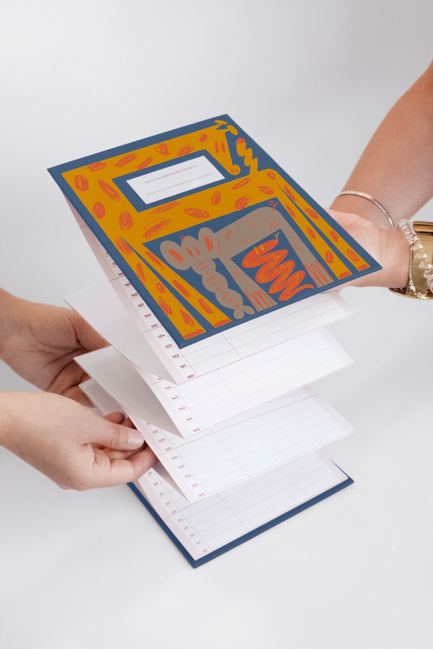 Zwei Personen halten einen offenen, bunten, mehrseitigen Kalender oder Planer mit linierten und datierten Abschnitten.