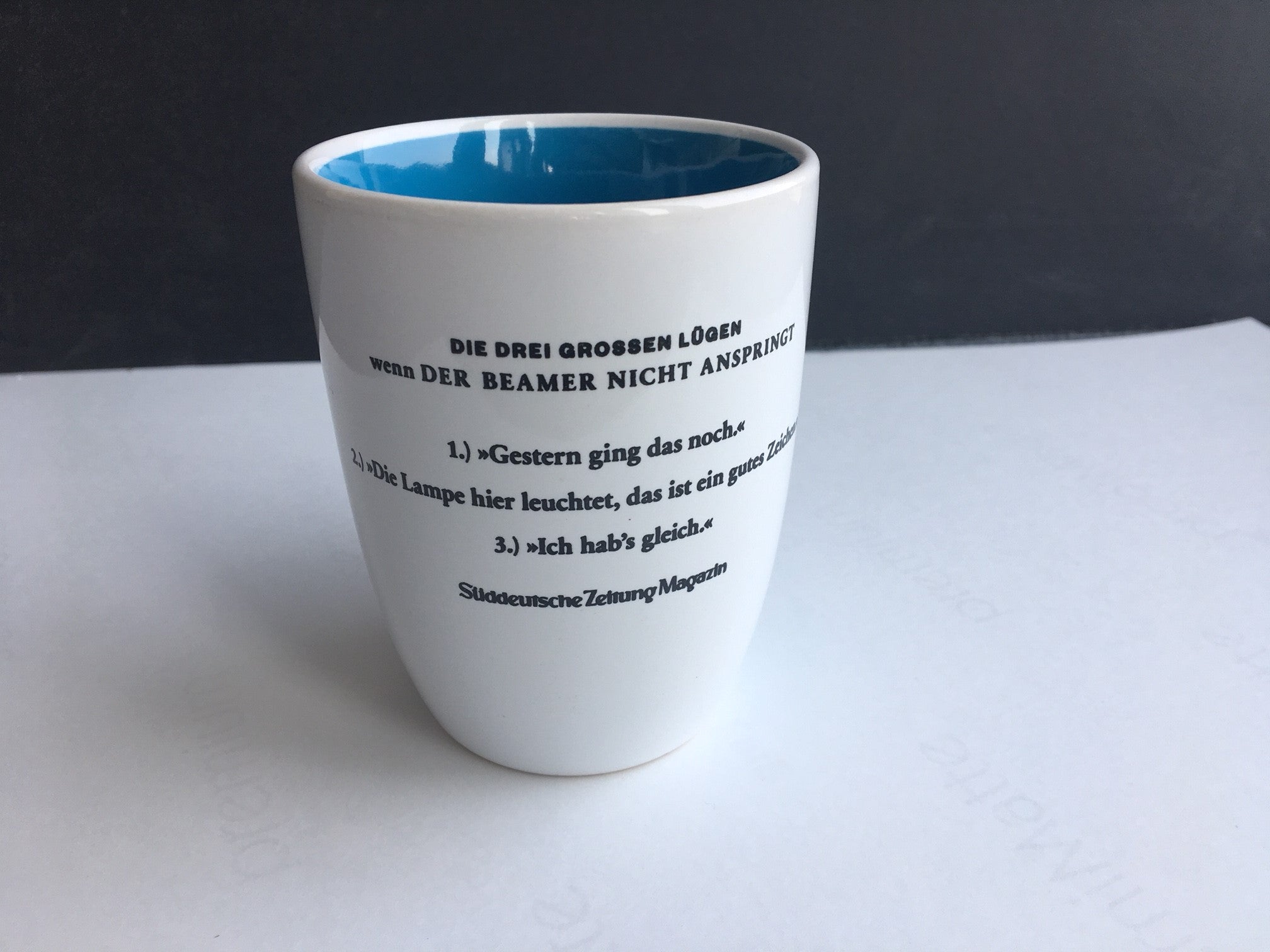 Weiße Tasse mit aufgedrucktem deutschen Text und einer Liste mit dem Titel „Die drei großen Lügen“.