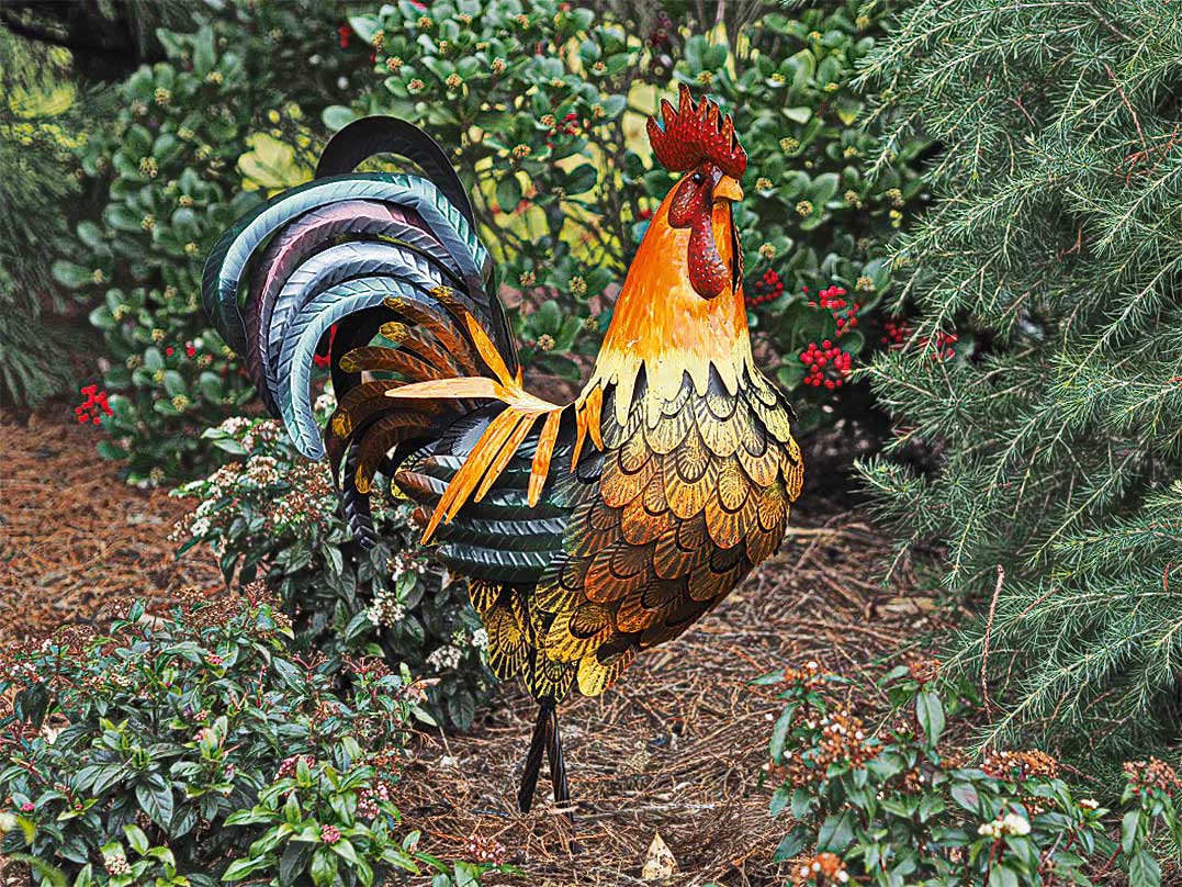 Eine farbenfrohe Hahnskulptur aus Metall steht in einem Garten, umgeben von grünen Pflanzen und roten Beeren.