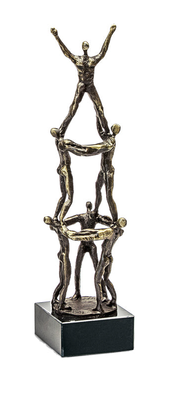 Bronzeskulptur von sechs menschlichen Figuren, die in Pyramidenformation auf einem schwarzen rechteckigen Sockel gestapelt sind.