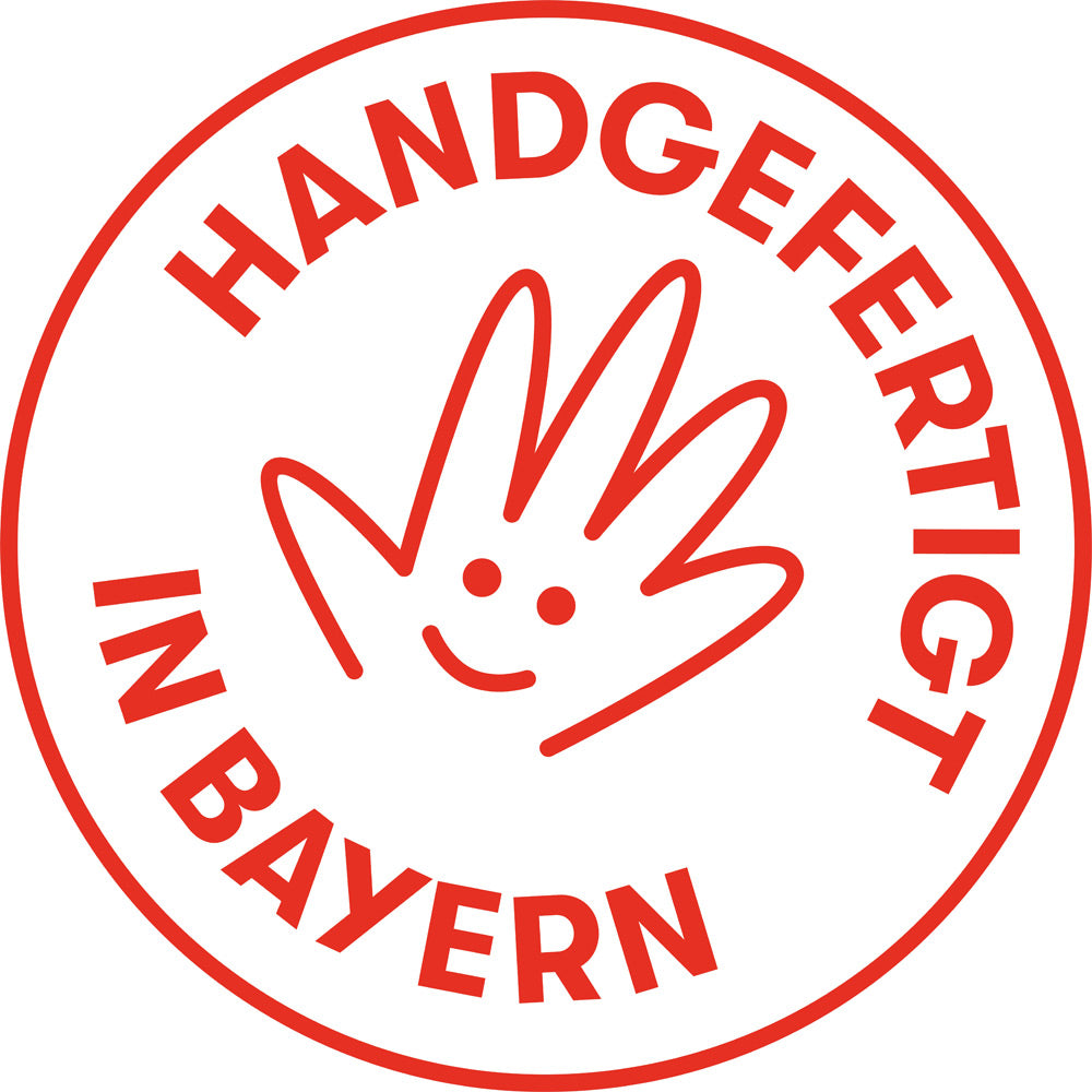 Roter Stempel mit einer lächelnden Handzeichnung und dem Text HANDGEFERTIGT IN BAYERN in einem Kreis.