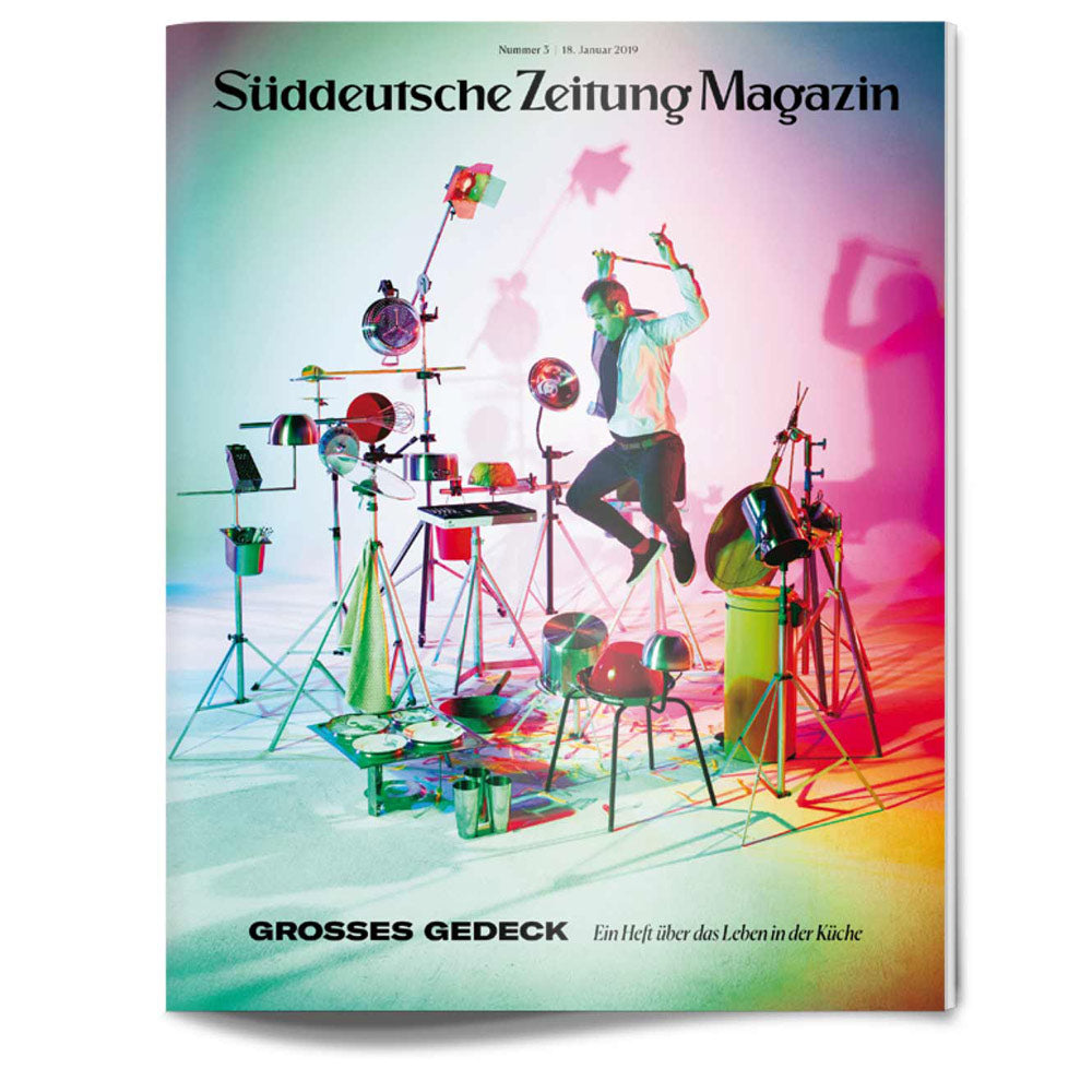 Ein Mann springt in einem farbenfrohen Studio, das mit Küchengeräten gefüllt ist, die wie ein Schlagzeug angeordnet sind, durch die Luft.