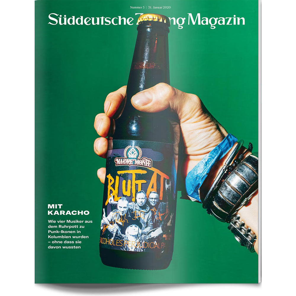 Eine Hand mit Armbändern hält eine "Blutfat"-Bierflasche vor einem grünen Hintergrund.
