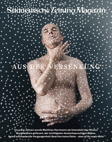 Ein glatzköpfiger, mit weißen Punkten bedeckter Mann posiert vor einem gepunkteten Hintergrund, Textüberlagerung in Deutsch.