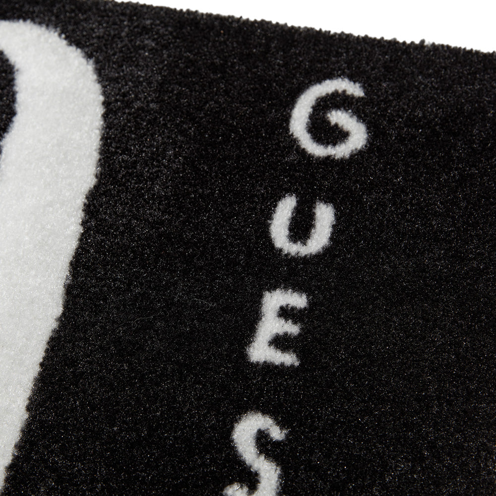 Nahaufnahme einer schwarzen strukturierten Oberfläche mit dem vertikal in weißen Buchstaben geschriebenen Wort GUESS.