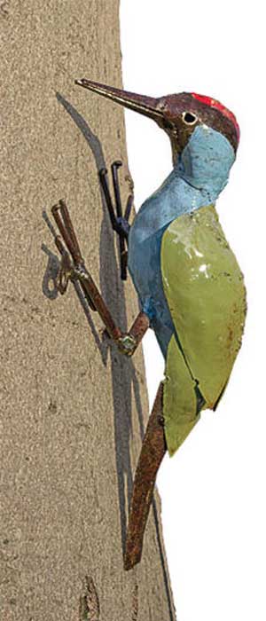 Eine farbenfrohe Vogelskulptur aus Metall in Form eines Spechts, die an einem Baumstamm befestigt ist.