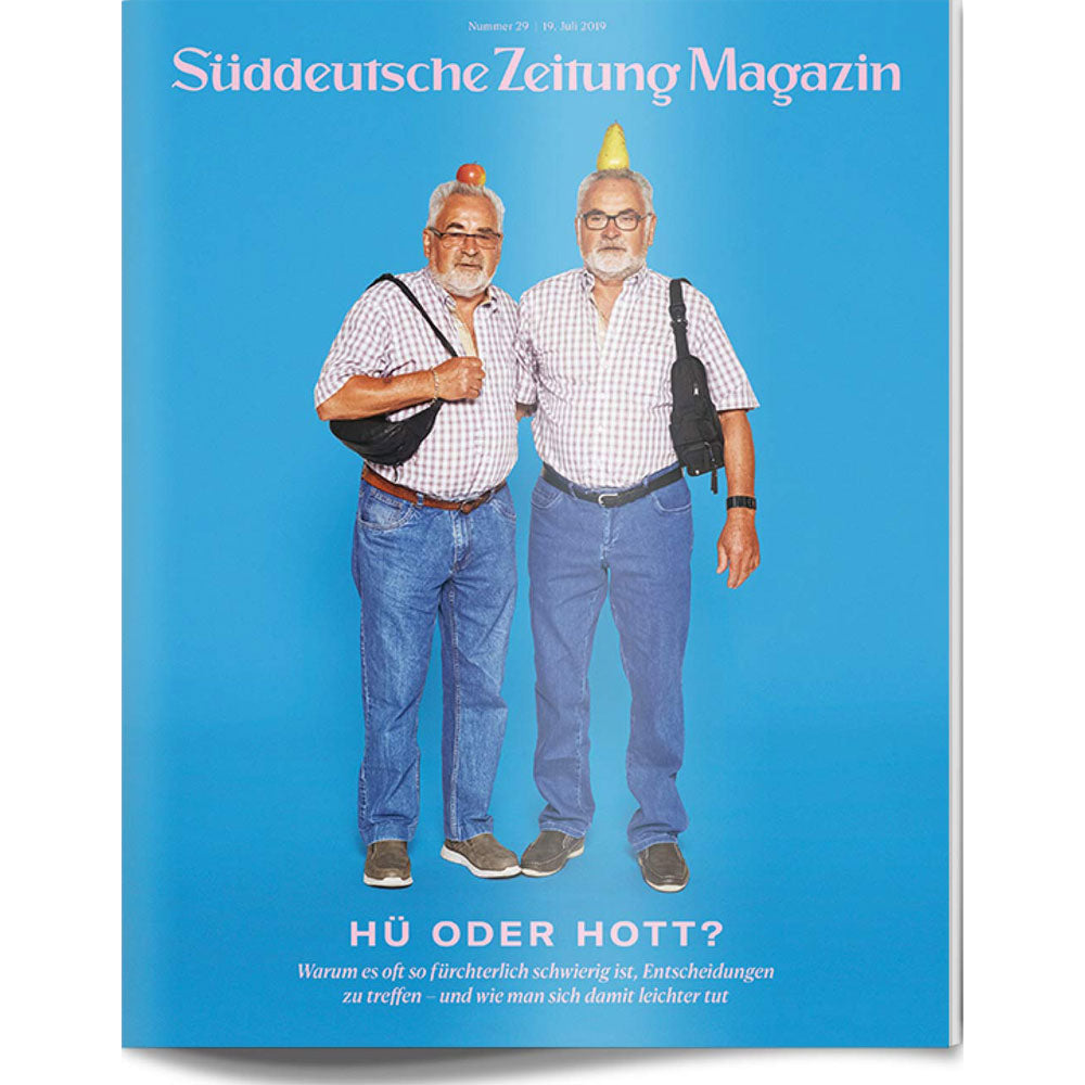 Zwei ältere Männer in passender Kleidung und ähnlichen Posen stehen zusammen vor einem blauen Hintergrund, jeder mit einer Frucht auf dem Kopf.