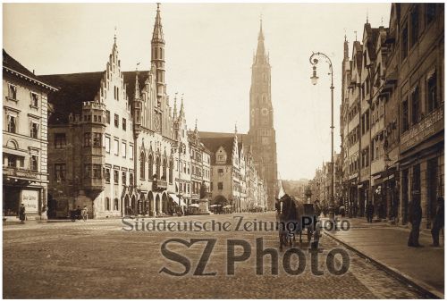 Historisches Sepia-Foto einer europäischen Stadtstraße mit gotischen Gebäuden und einem hohen Kirchturm im Hintergrund.