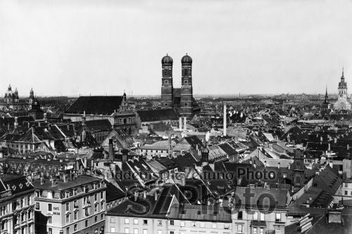 Schwarz-weißes Stadtbild von München mit den Zwillingskuppeln der Frauenkirche über historischen Dächern.
