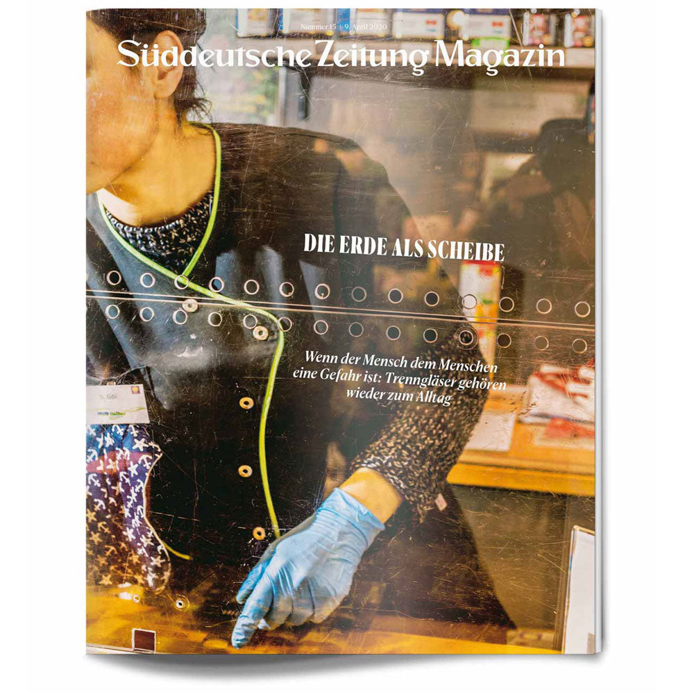 Eine Person in einem schwarzen Mantel und blauen Handschuhen steht hinter einer Glasscheibe mit kreisförmigen Mustern auf einem Zeitschriftencover.