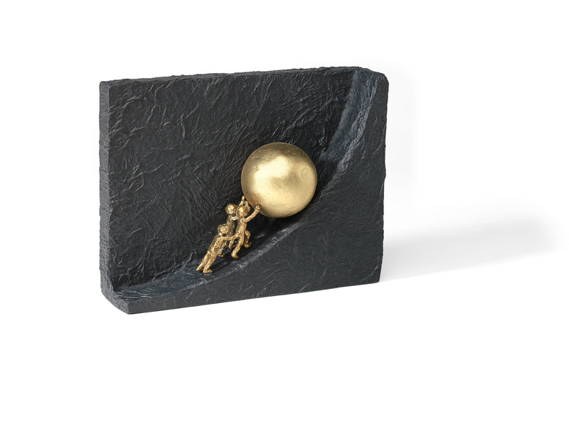 Eine kleine goldene Figur schiebt eine goldene Kugel über eine strukturierte schwarze rechteckige Oberfläche.