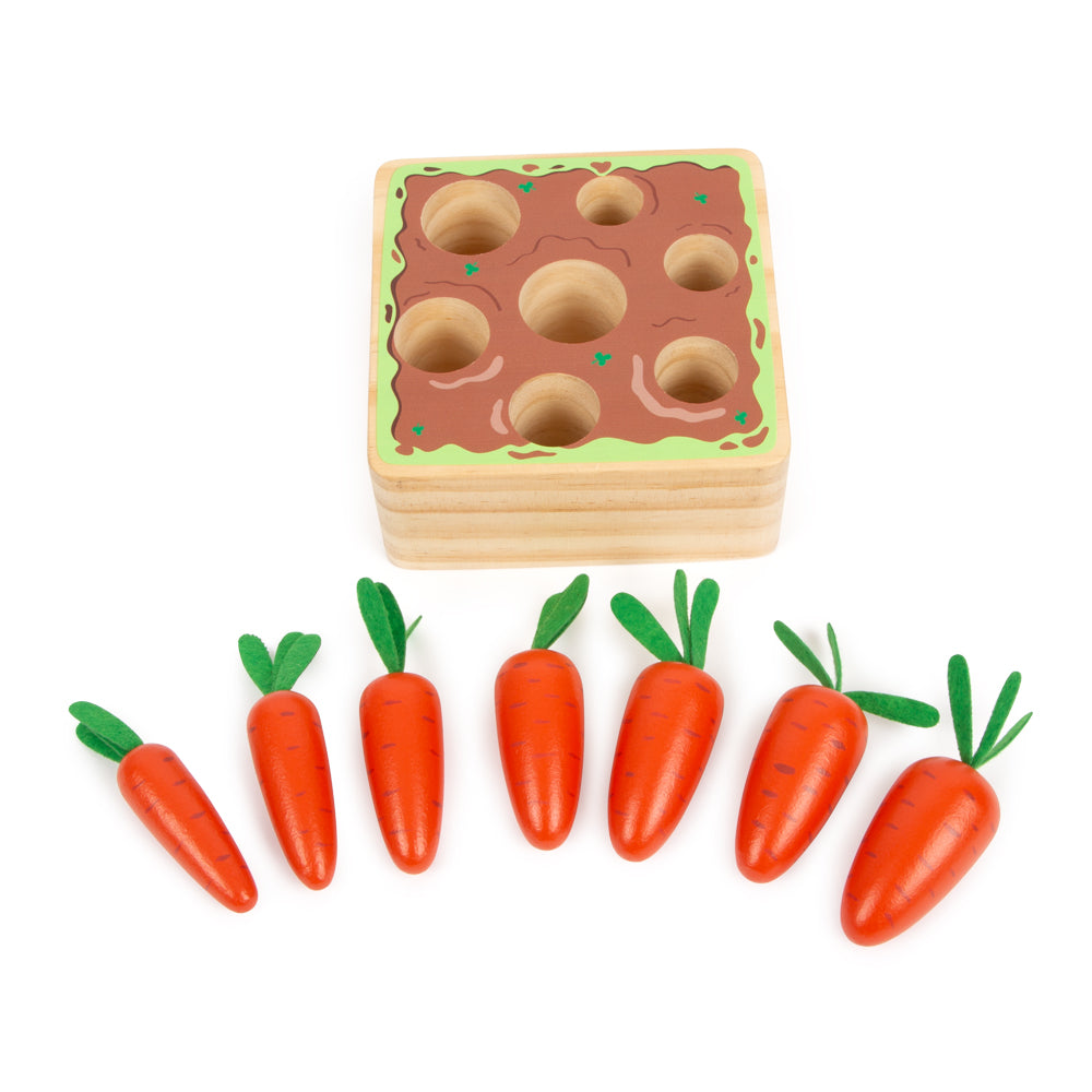 Steckspiel Möhren ist ein Holzspielzeug mit Löchern und sieben herausnehmbaren Spielmöhren mit grünen Filzblättern.
