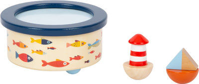 Spieluhr Großer Ozean: Runde Spielzeugtrommel mit buntem Fischmotiv, daneben ein kleiner Leuchtturm und ein Spielzeugboot.