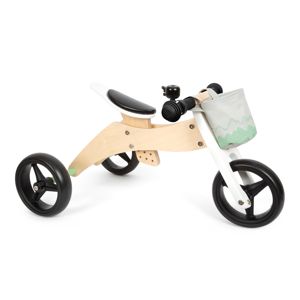 Das Lauf- und Dreirad Salbeigrün ist ein weißes Holzdreirad mit schwarzen Rädern, einer kleinen Klingel und einem grauen Vorderkorb mit grüner Verzierung.