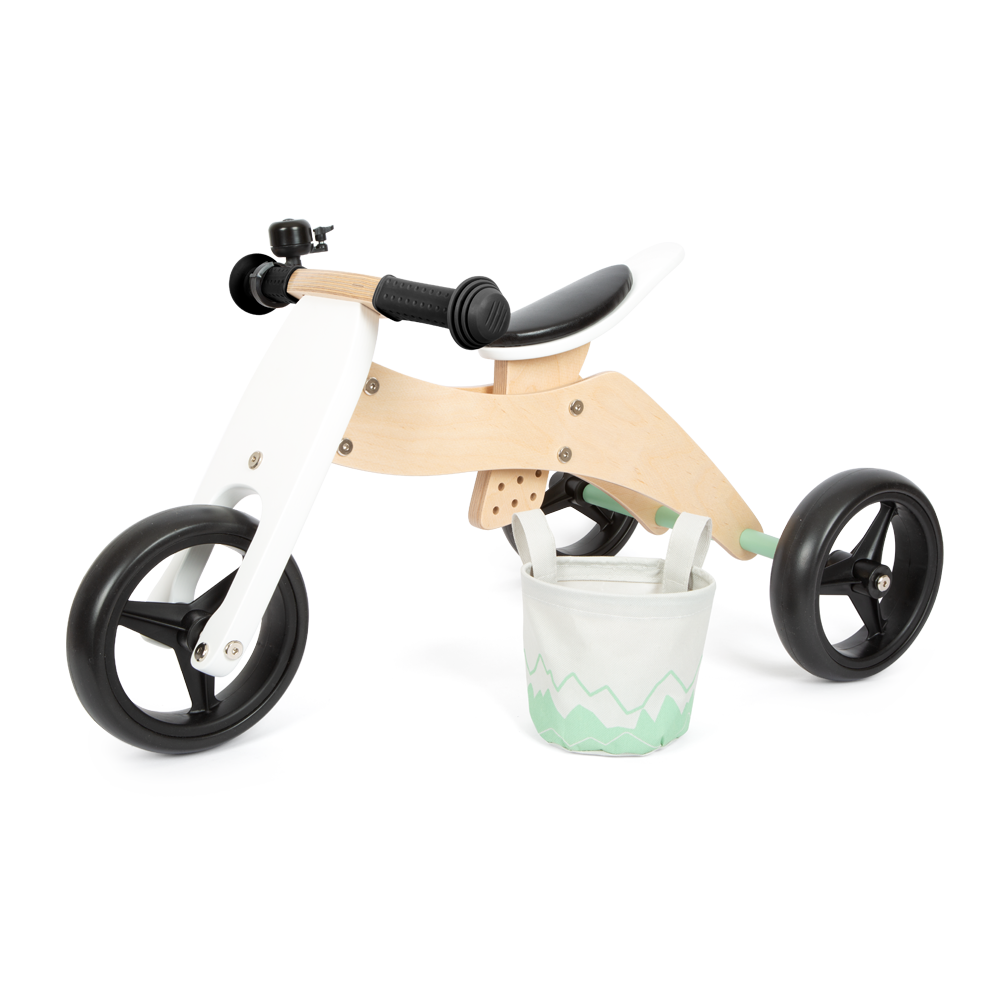 Das Lauf- und Dreirad Salbeigrün ist ein hölzernes Kleinkinddreirad mit schwarzen Rädern, einem schwarzen Sitz und einem kleinen dekorativen Vorderkorb.