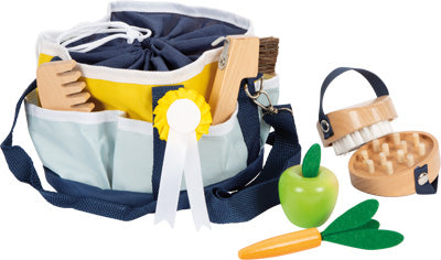 Die Pferdepflege-Tasche ist ein Spielzeug-Pflegeset mit Holzbürsten, einem grünen Apfel, einer orangefarbenen Karotte und einer blau-gelben Tasche mit Taschen.