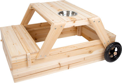 Sandkasten mit Sitzgruppe und Matschtisch: Holz-Picknicktisch mit integrierten Bänken, schwarzen Rädern und einer Metallschüssel in der Tischmitte.