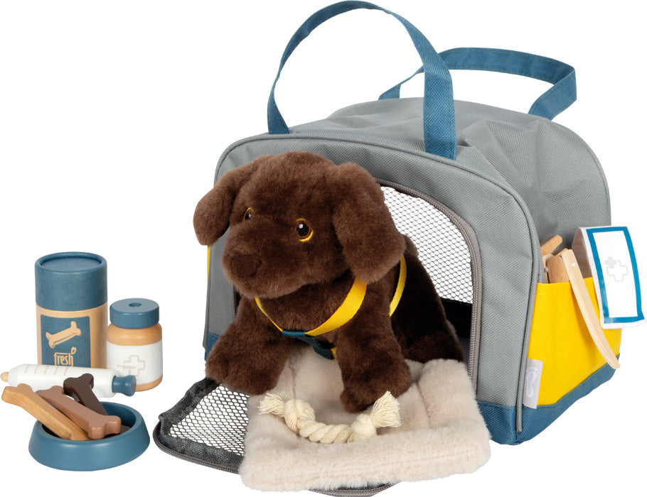 Das „Hund mit Tasche und Pflege-Set“ beinhaltet einen braunen Plüschhund in einer grauen Tragetasche mit Spielzeugfutter, Napf, Seil und Pflegezubehör daneben.