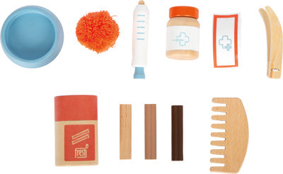 Das „Katze mit Tasche und Pflege“-Set enthält ein Spielzeug-Tierarzt-Set mit medizinischen Instrumenten aus Holz, einem Kamm, einer Schüssel, Verbänden, einer Tablettenflasche und einem orangefarbenen Pompon.