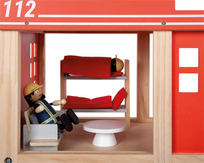 Feuerwehrpuppen aus Holz ruhen auf Etagenbetten und einem Stuhl in einer roten Spielzeug-Feuerwache.