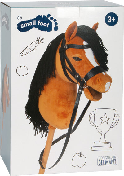 Schachtel mit einem Spielzeug-Steckenpferd mit schwarzer Mähne, schwarzem Zaumzeug und Abbildungen einer Karotte, eines Apfels und einer Trophäe.