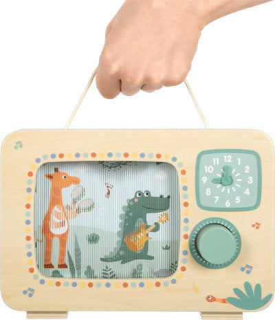Eine Hand hält einen Spielzeugfernseher aus Holz, auf dessen Bildschirm eine Giraffe und ein Krokodil Instrumente spielen.