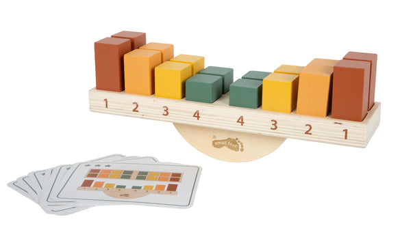 Balancierspielzeug aus Holz mit farbigen Blöcken und nummerierten Schlitzen sowie passenden Musterkarten daneben.