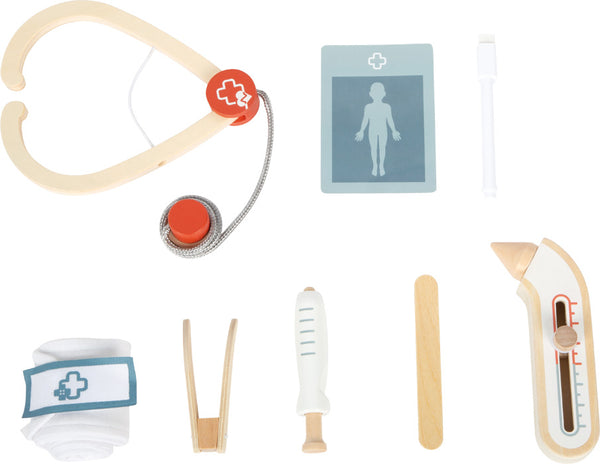Ein Satz medizinischer Spielzeuginstrumente, darunter ein Stethoskop, ein Röntgengerät, eine Spritze, ein Thermometer, ein Zungenspatel, eine Salbentube, eine Pinzette und ein Verband, angeordnet auf einem weißen Hintergrund.