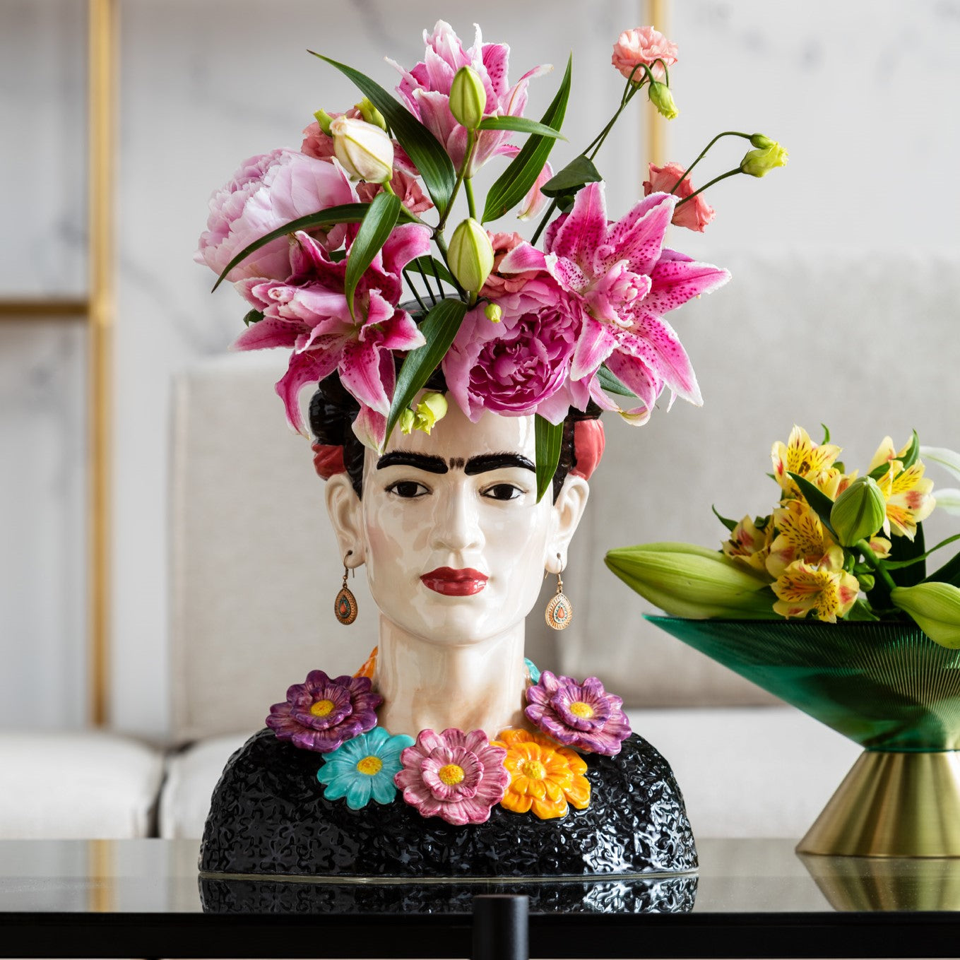 Die Deko Vase Style Muse Flowers zeigt Frida Kahlos Kopf mit pinken Blumen, markanten Augenbrauen und auffälligen Ohrringen – daneben steht eine Frauentorso-Vase, geschmückt mit gelben Blumen.