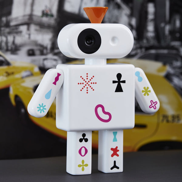 Weißer Spielzeugroboter mit bunten Symbolen steht vor einer verschwommenen Stadtszene mit gelben Taxis.