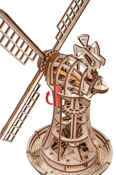 Holzmodell einer Windmühle mit sichtbaren Zahnrädern und rotierenden Flügeln, mit einem roten Pfeil, der die Richtung angibt, in die eine Kurbel zu drehen ist.
